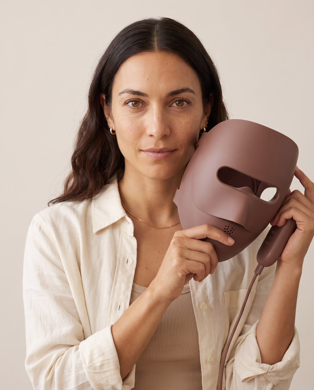 Clinaray LED mask in Brown held up unlit next to the face, showing the open eye window, the breathing holes below the nose and the handheld controller