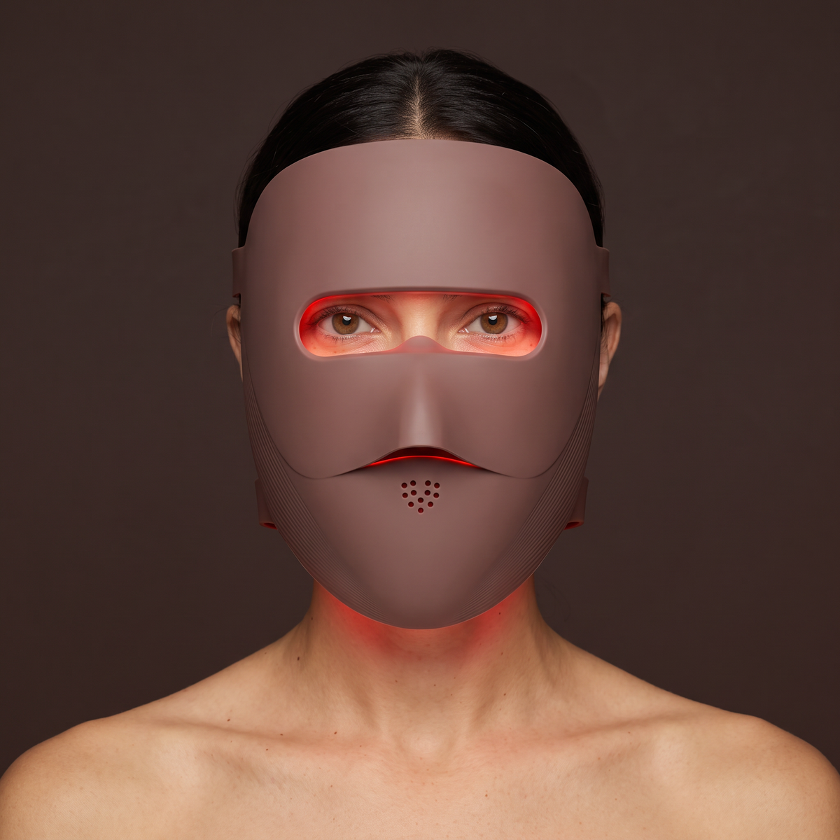 Close-up of the Clinaray LED mask in Brown worn with red mode on, the red light showing only through the open eye window. Close your eyes or use shields if the light bothers you.